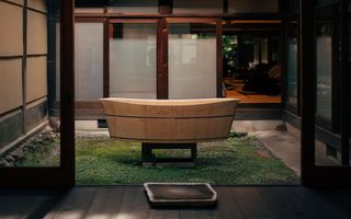 A wooden hinoki bathtub standing on moss in the courtyard of a traditional Japanese house