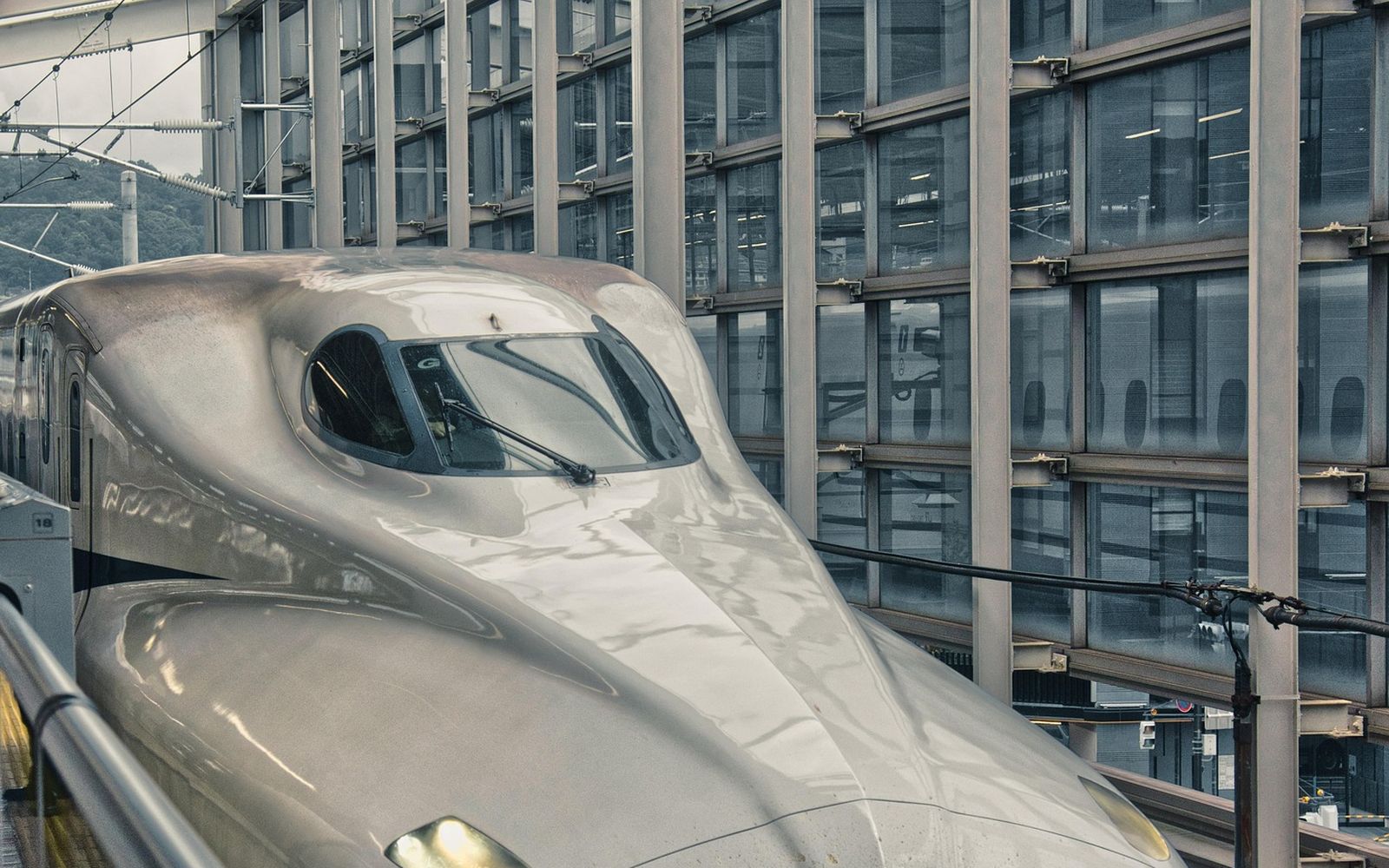 The nose of a shinkansen waiting at a platform, with the station's glass wall behind it