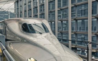 The nose of a shinkansen waiting at a platform, with the station's glass wall behind it